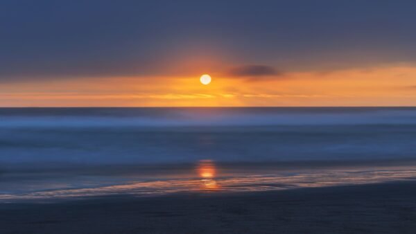 A tranquil sunset viewed over Chilca Beach, Peru, with vibrant ocean colors.
